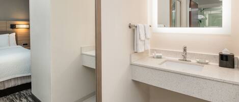 A hotel bathroom with a bed, a sink, a mirror, and a towel rack.