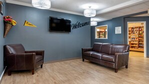 Een receptiegedeelte met een bruine leren bank, een bruine fauteuil, een bord met de tekst 'Welcome', een 'Hornets' banner, een flatscreen televisie en een bord dat de weg wijst naar de eetruimte.