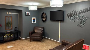 Een receptiegedeelte met een leren bank, een stoel, een console tafel met decoratieve objecten, een tv aan de muur en een bord met de tekst 'Welcome' met een ontwerp van een boom.