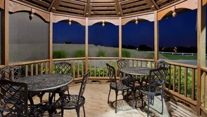 Een overdekt terras buiten met houten leuningen en metalen tafels en stoelen.