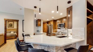 A modern kitchen with a large island, stainless steel appliances, and dark wooden cabinets. - The Charter at Beaver Creek (Avon)