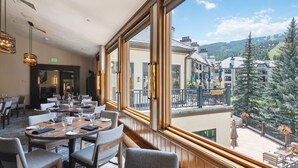 A restaurant with tables set for dining, large windows offering a view of buildings and trees. - The Charter at Beaver Creek (Avon)