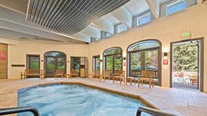 A pool area with a hot tub, wooden chairs, and a view of the outdoors through arched doors. - The Charter at Beaver Creek (Avon)