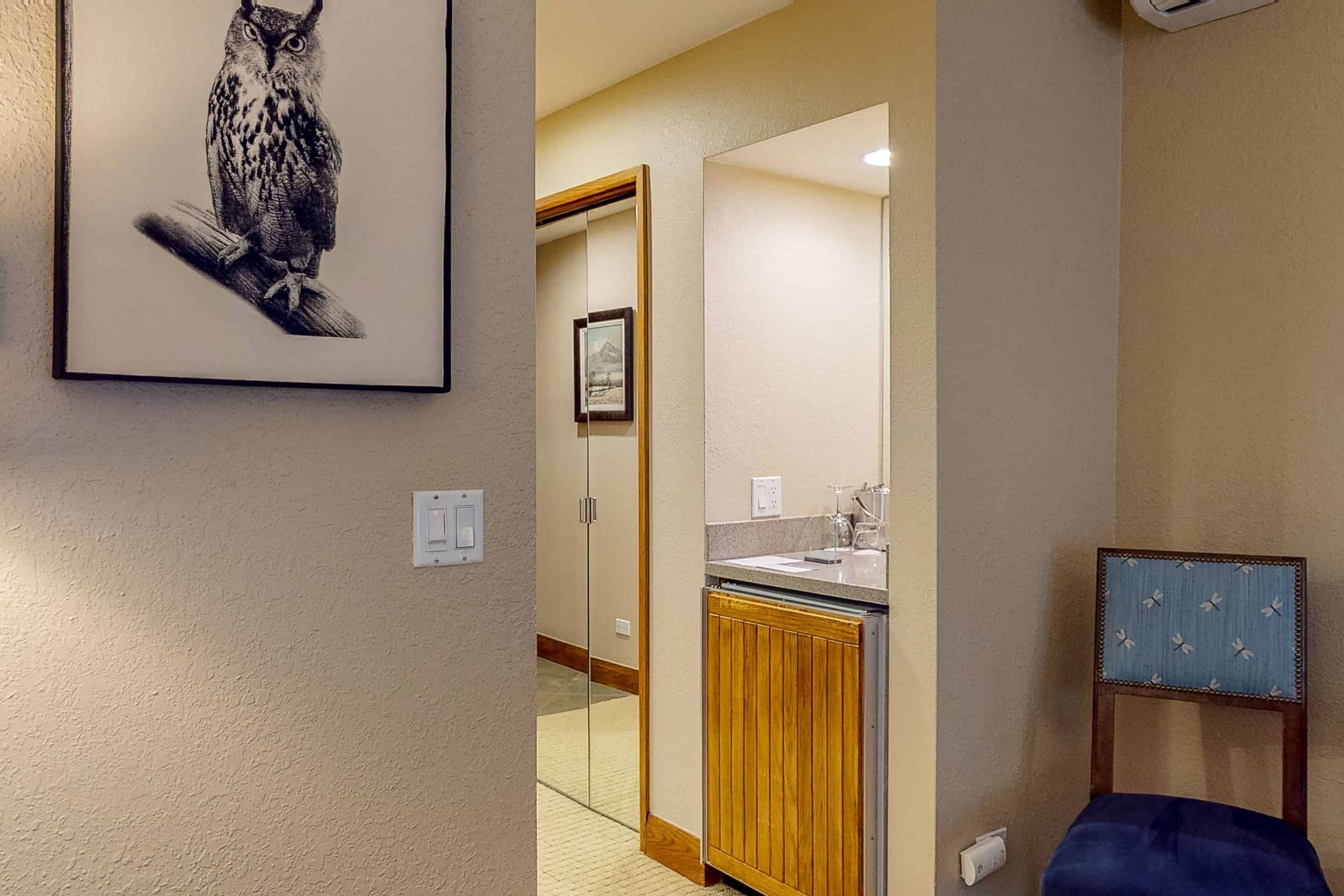A hallway with a framed owl artwork, a wooden cabinet, a mirror, and a blue chair.