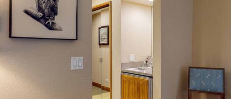 A hallway with a framed owl artwork, a wooden cabinet, a mirror, and a blue chair.