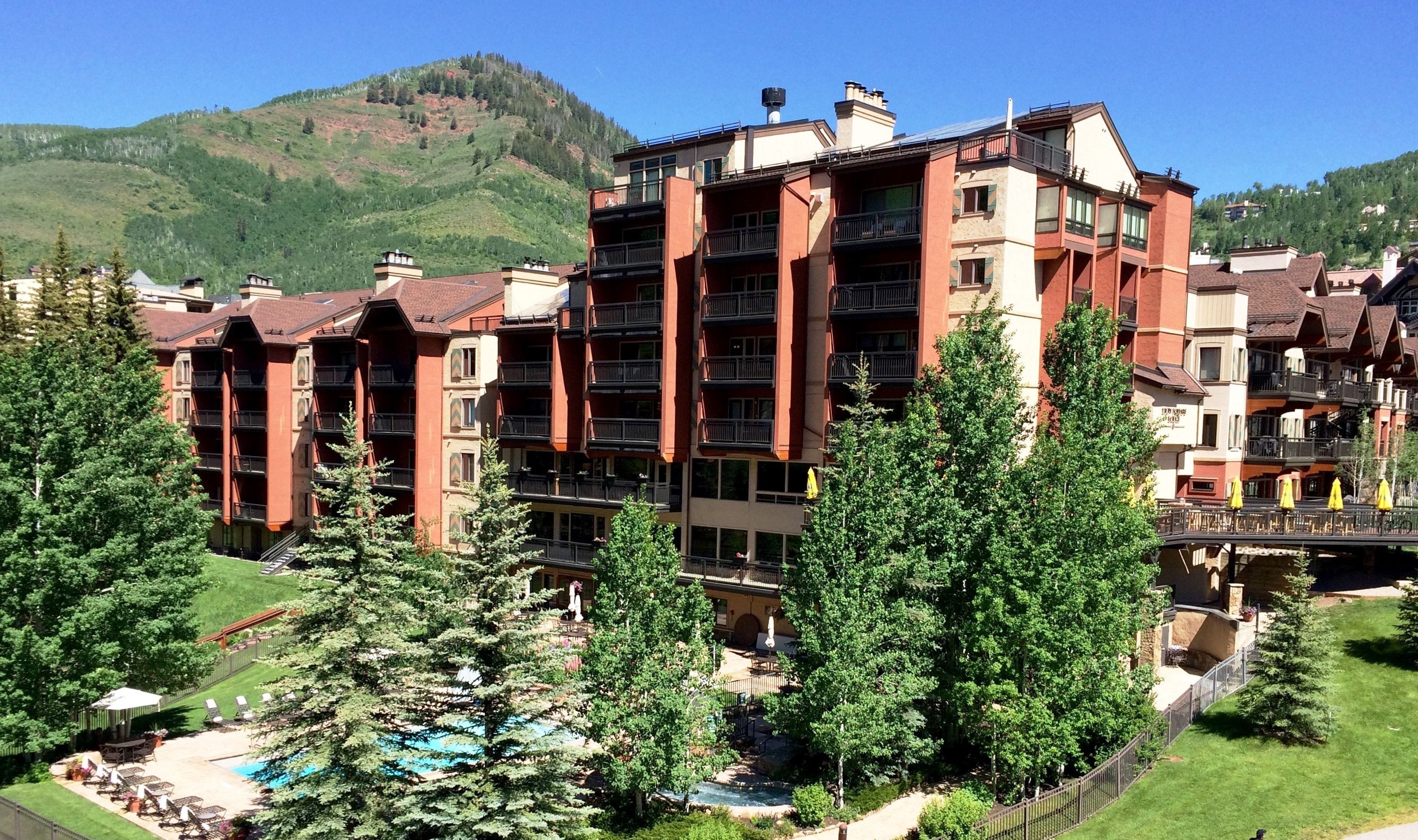 A multi-story hotel with balconies, a pool area, and a mountain backdrop.