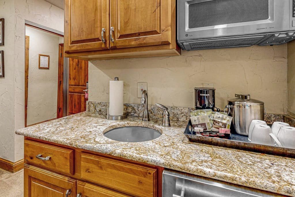 A kitchen with wooden cabinets, a granite countertop, a stainless steel sink, a microwave, and a coffee maker.