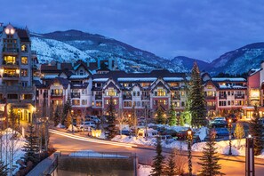 A hotel with multiple floors, a parking lot, and snow-covered mountains in the background.