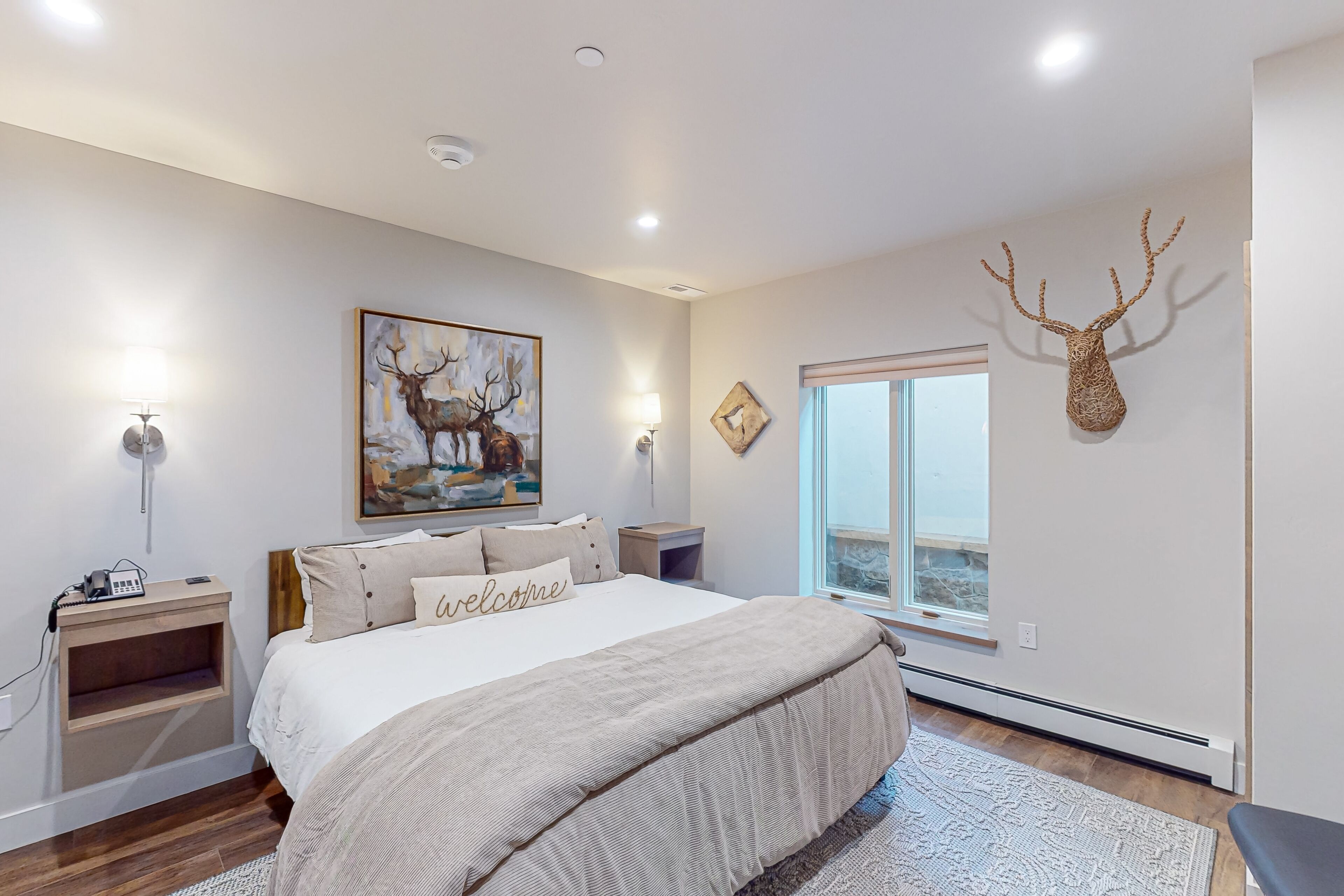 Een slaapkamer met een groot bed, een decoratie van een hertenkop, een schilderij van herten en een raam met uitzicht.