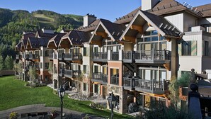 Un hotel de varios pisos con balcones, un césped bien cuidado y vistas a una ladera boscosa.