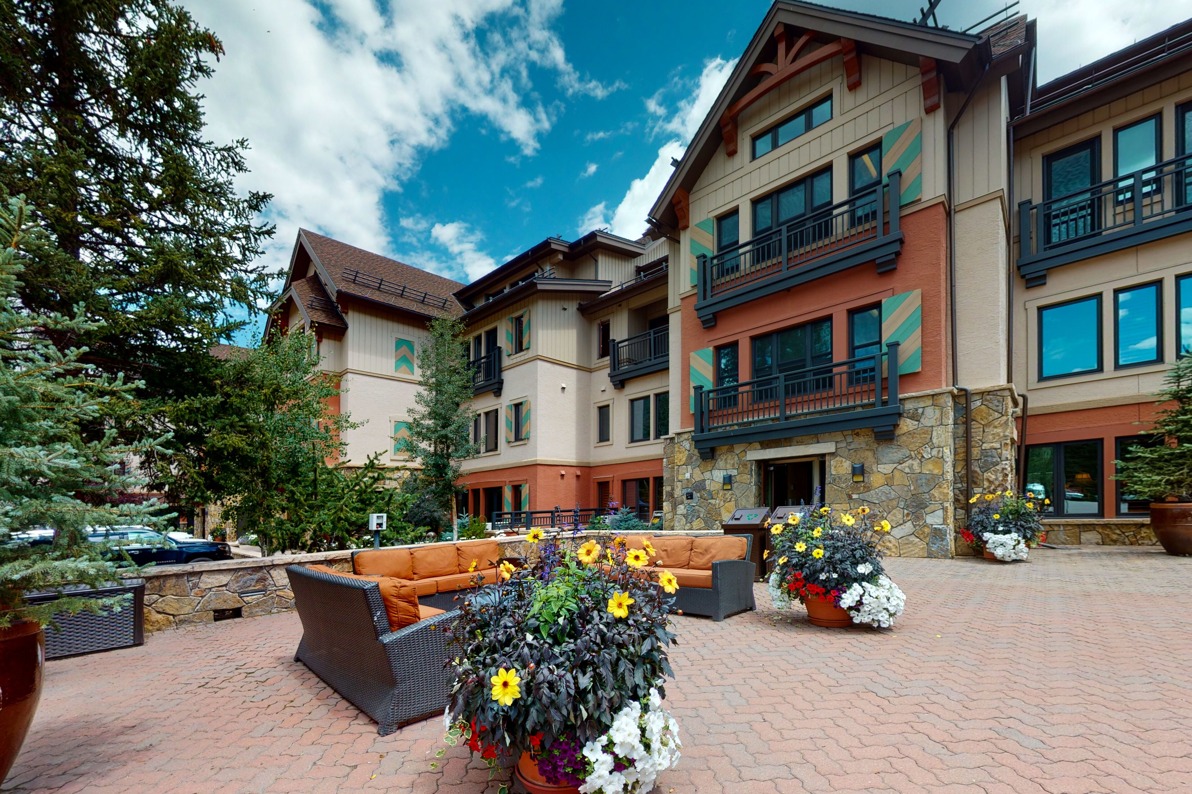A hotel courtyard with outdoor seating, potted plants, and a stone wall.