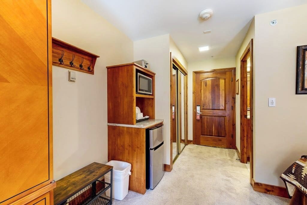 A narrow hallway with a wooden cabinet, a refrigerator, and a microwave.