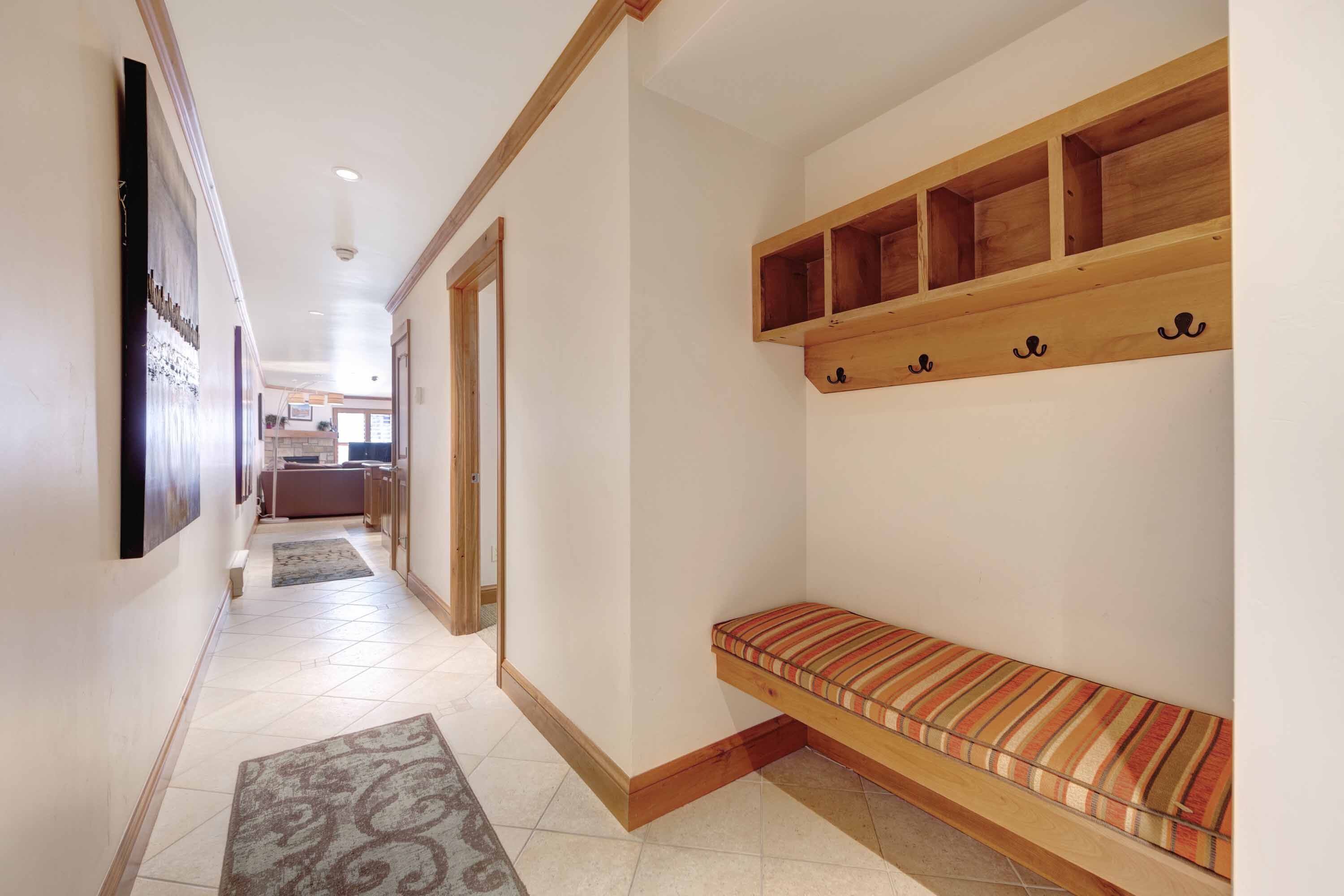 A hallway with a bench, a wooden shelf with hooks, and a patterned rug.