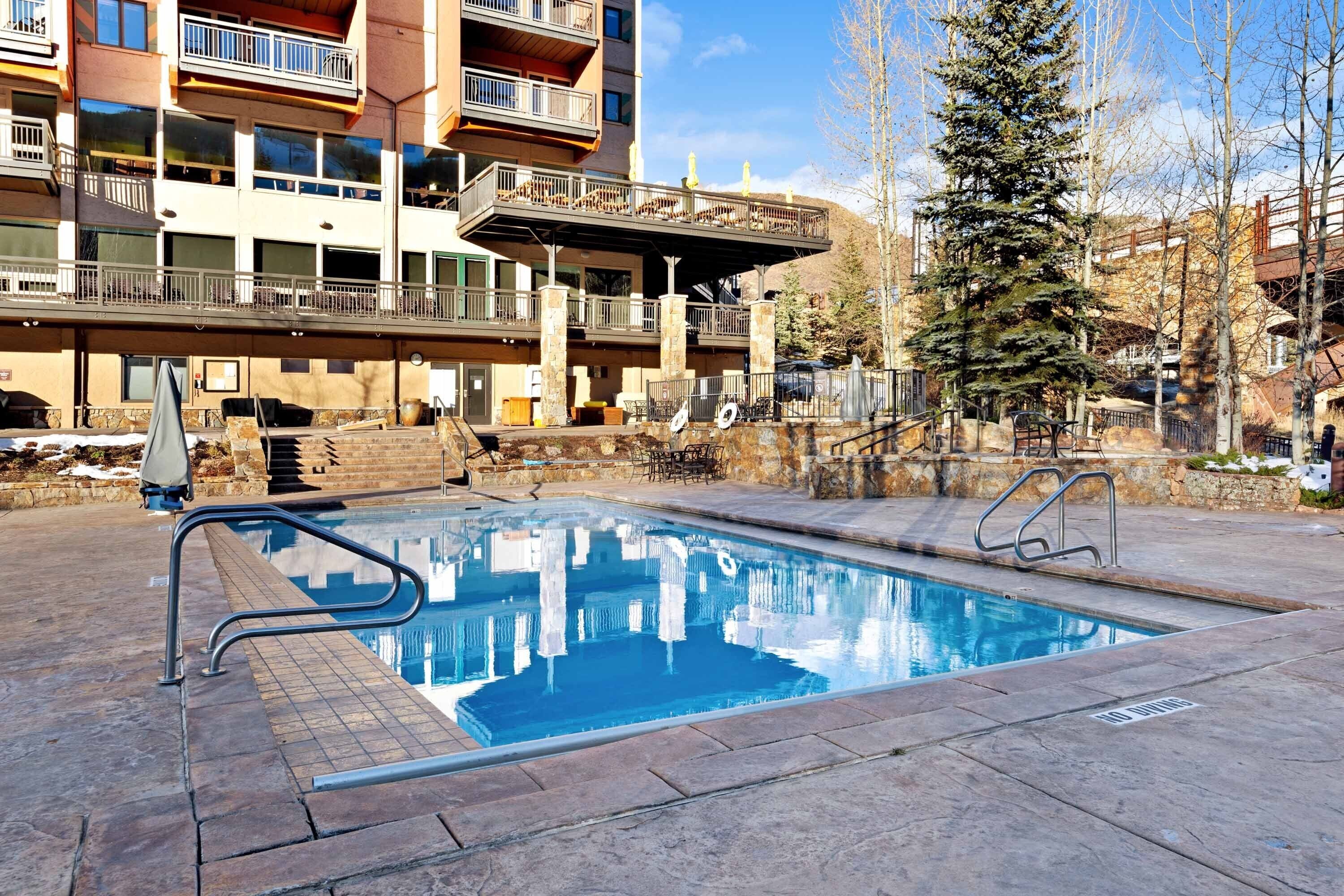 A swimming pool with a clear blue water surface, surrounded by stone tiles.