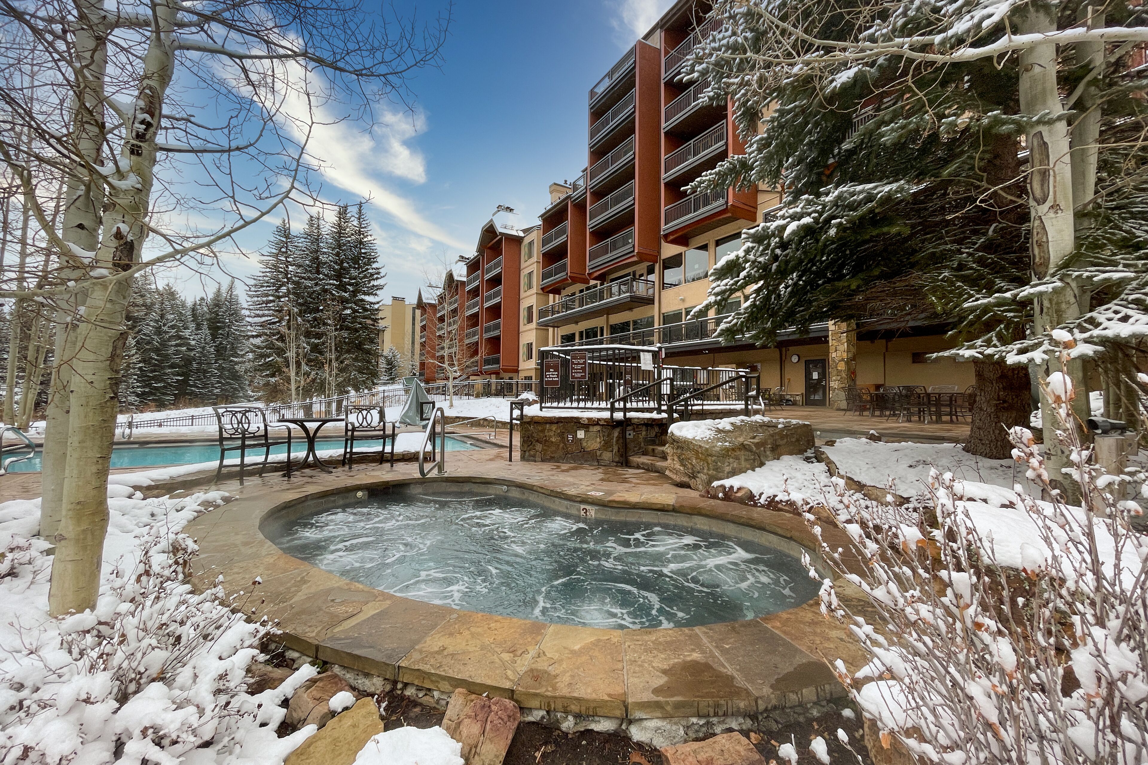 Un espace extérieur enneigé comprenant un jacuzzi, une piscine et un bâtiment doté de plusieurs balcons.