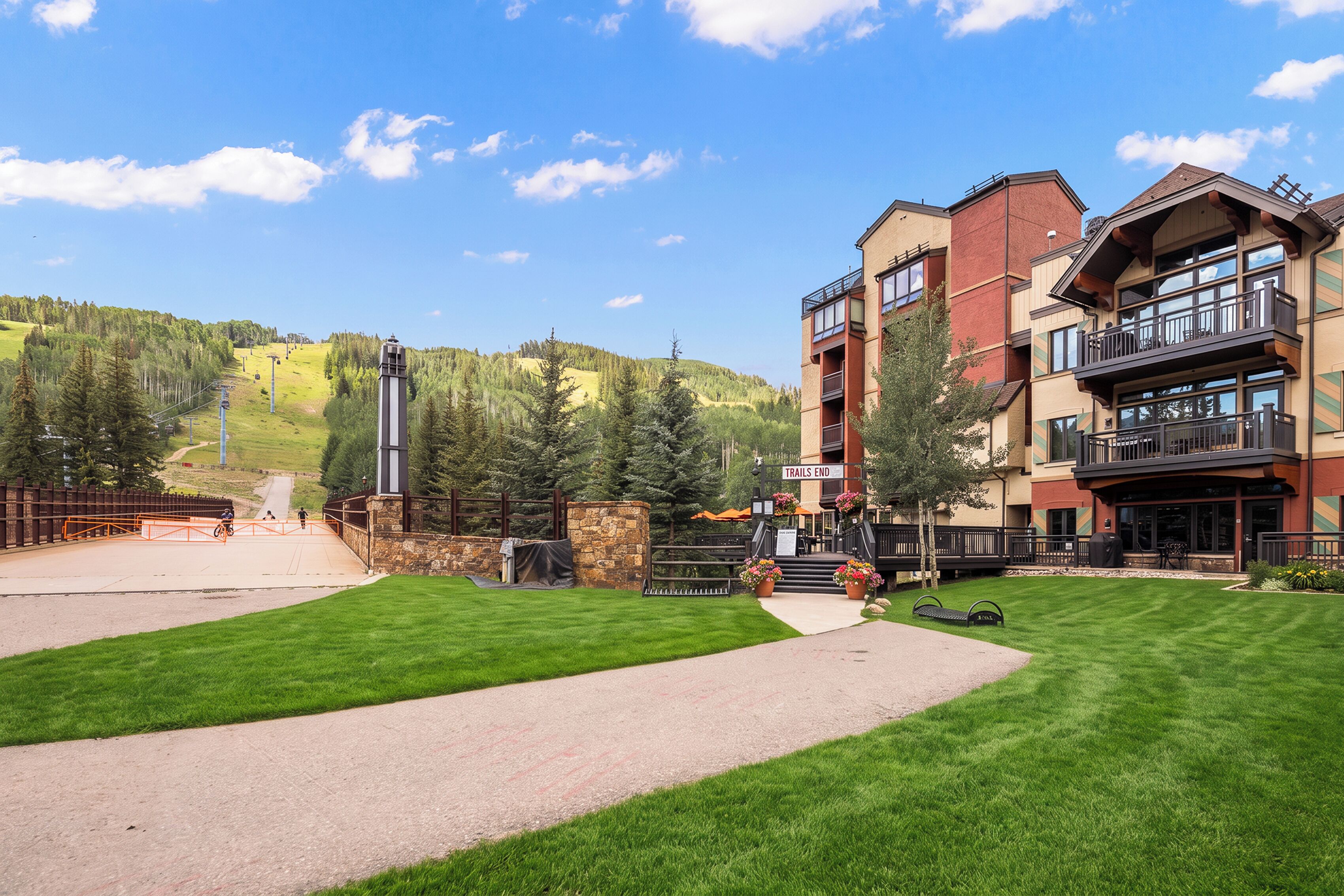 A hotel with a paved walkway, a sign indicating the end of trails, and a mountainous backdrop.