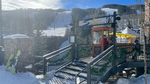 Un centro de esquí con un restaurante llamado 'el Saburant' y una zona nevada con una tabla de snowboard apoyada en una valla.