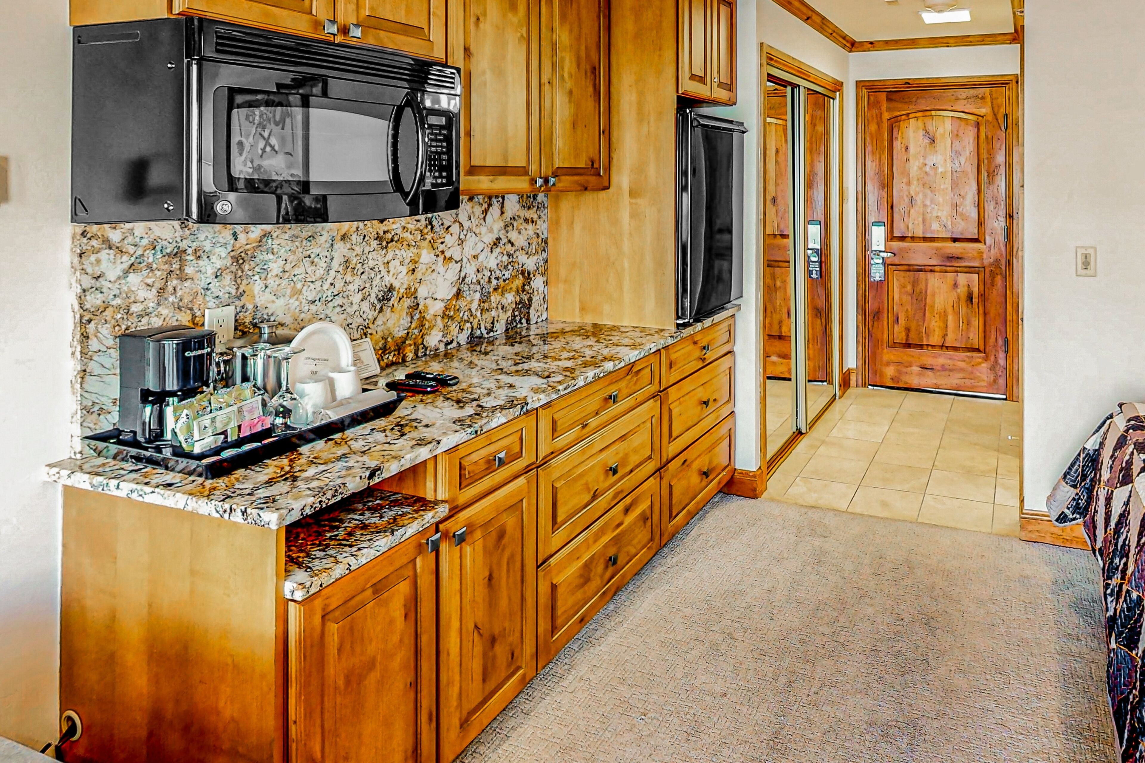 A kitchen with wooden cabinets, a granite countertop, a microwave, a refrigerator, and a coffee maker.