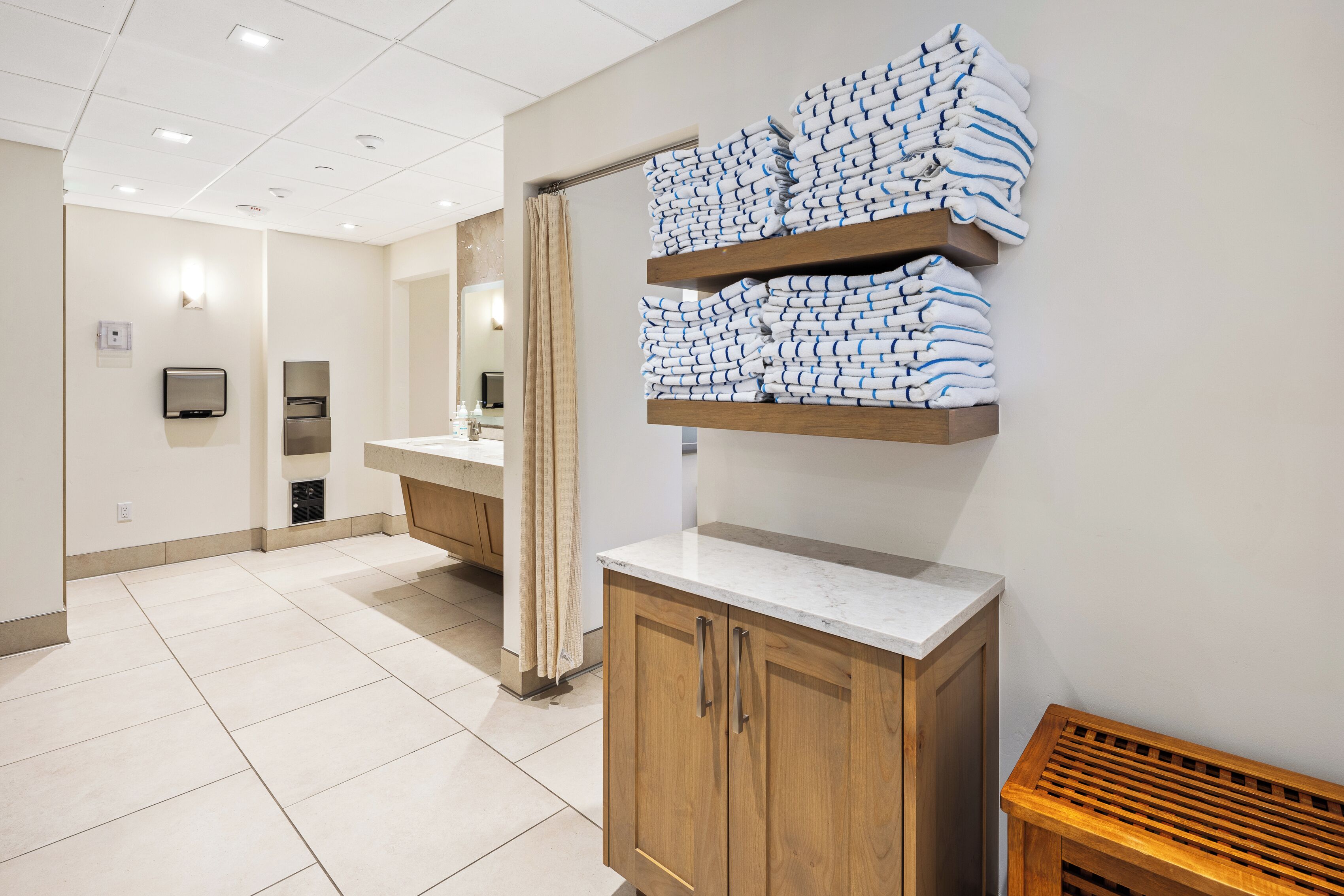 A hotel bathroom with a sink, mirror, towel rack, and a wooden bench.