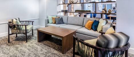 A modern living room with a grey sofa, patterned rug, wooden coffee table, and wicker chairs.