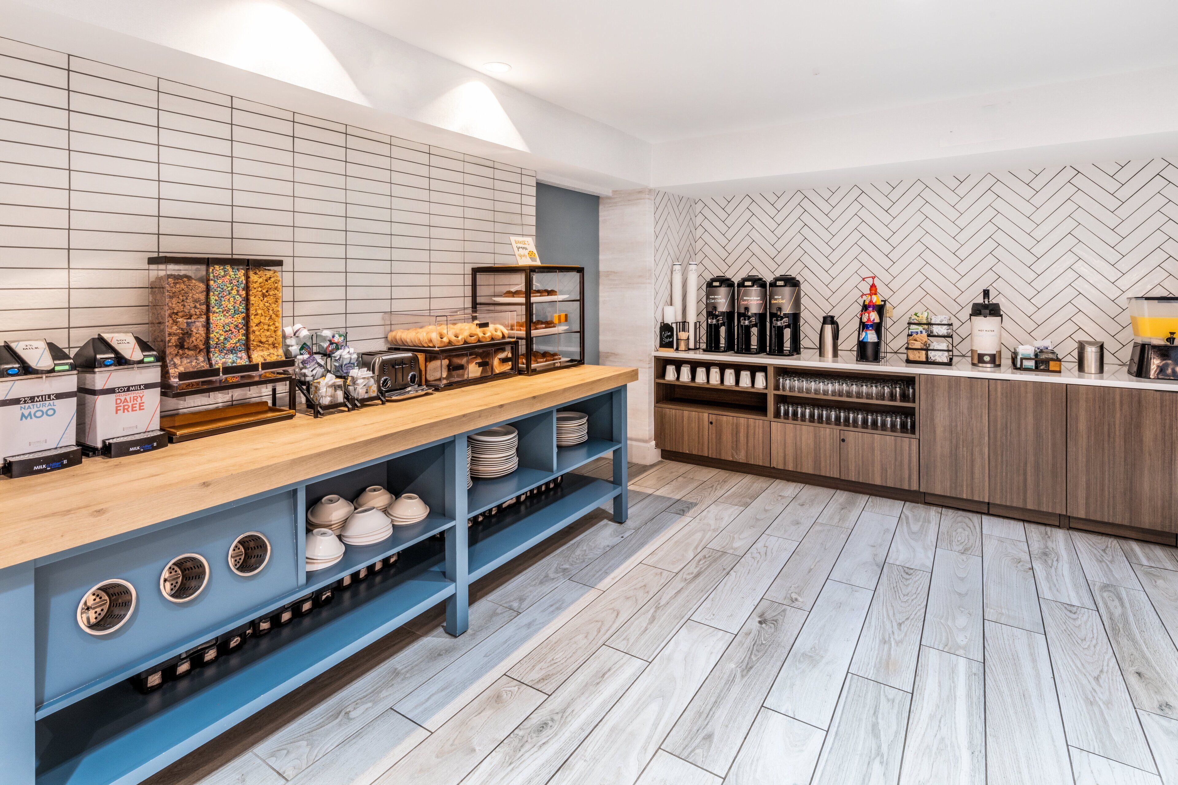 Ein modernes Café mit Holztresen, Regalen mit Optionen für haltbare Milchprodukte und Sojamilch sowie einer Kaffeestation mit diverser Brühapparatur.