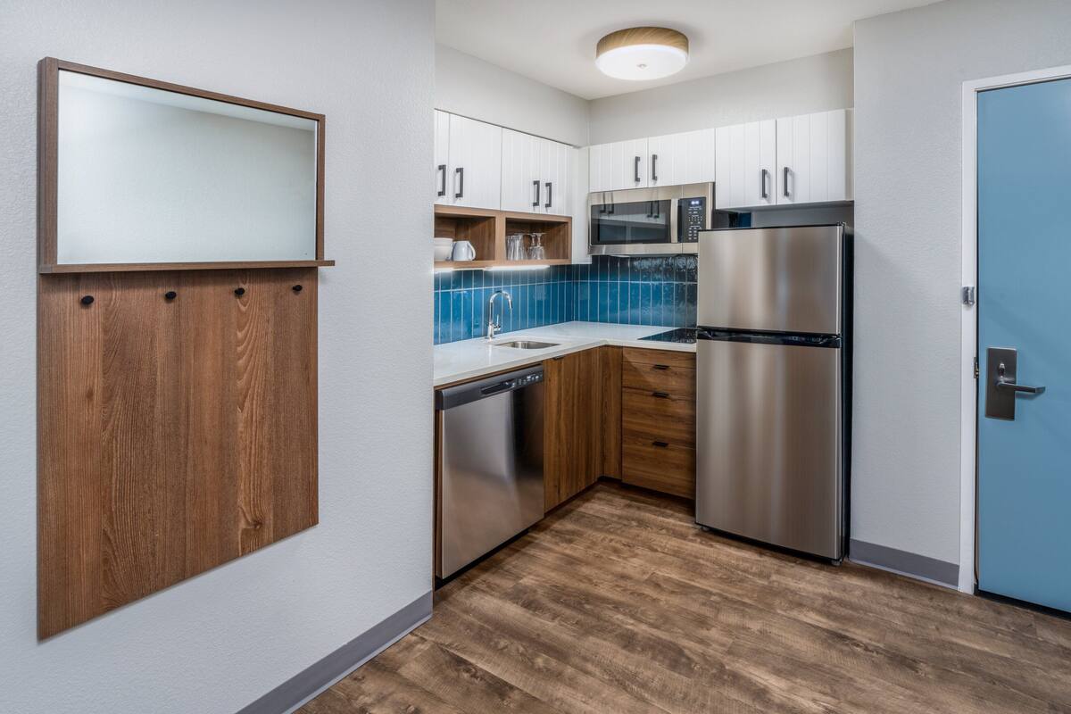A modern kitchen with white cabinets, a stainless steel refrigerator, a dishwasher, and a blue-tiled backsplash.
