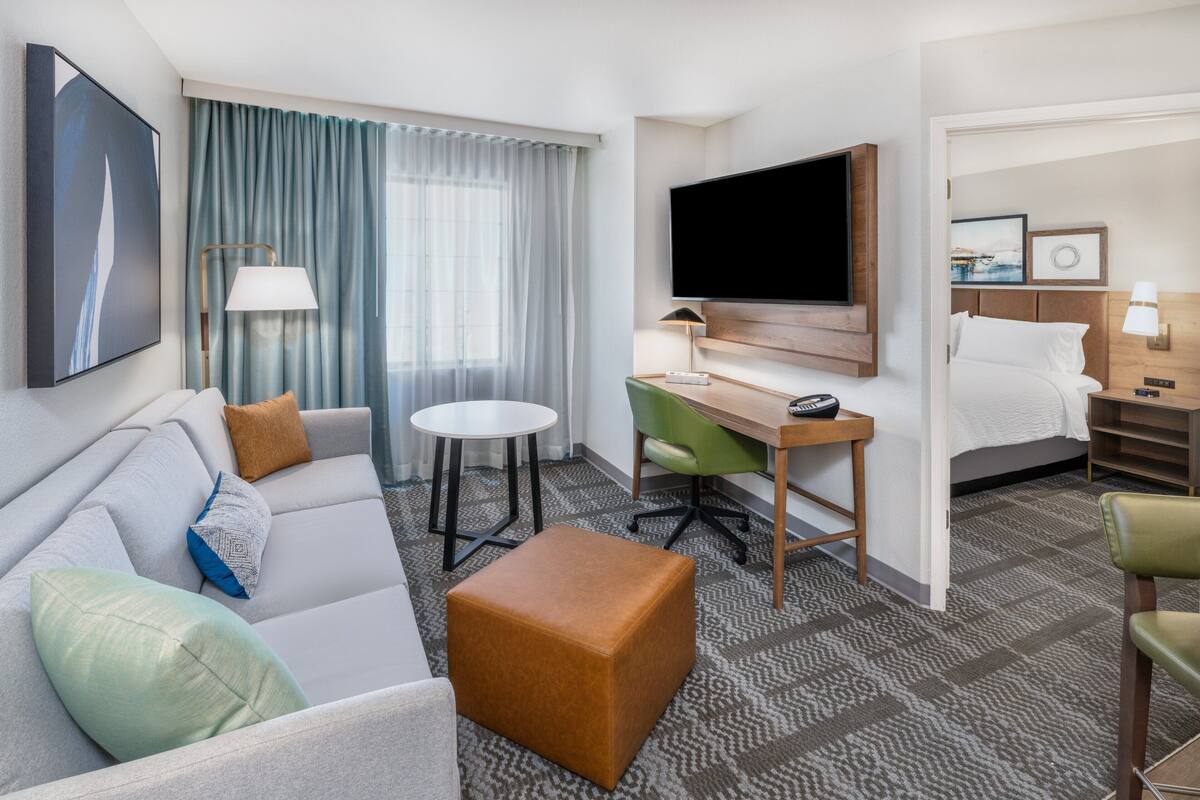 A hotel room with a sofa, a desk, a television, a bed, and a window with curtains.