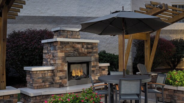 Eine Terrasse im Freien mit Kamin aus Stein, einem runden Tisch und Stühlen.