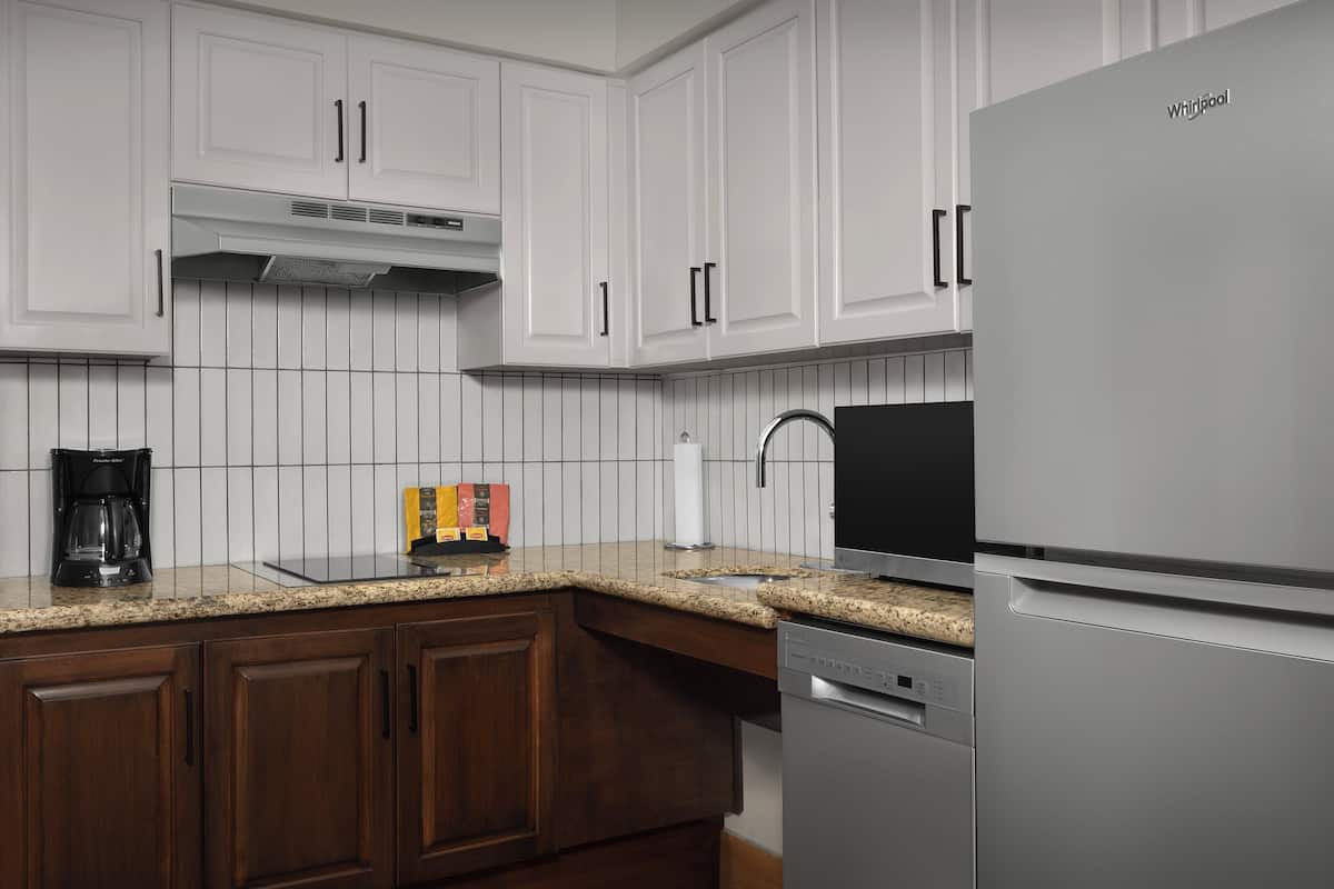 A modern kitchen with white cabinetry, a stainless steel refrigerator, and a granite countertop.