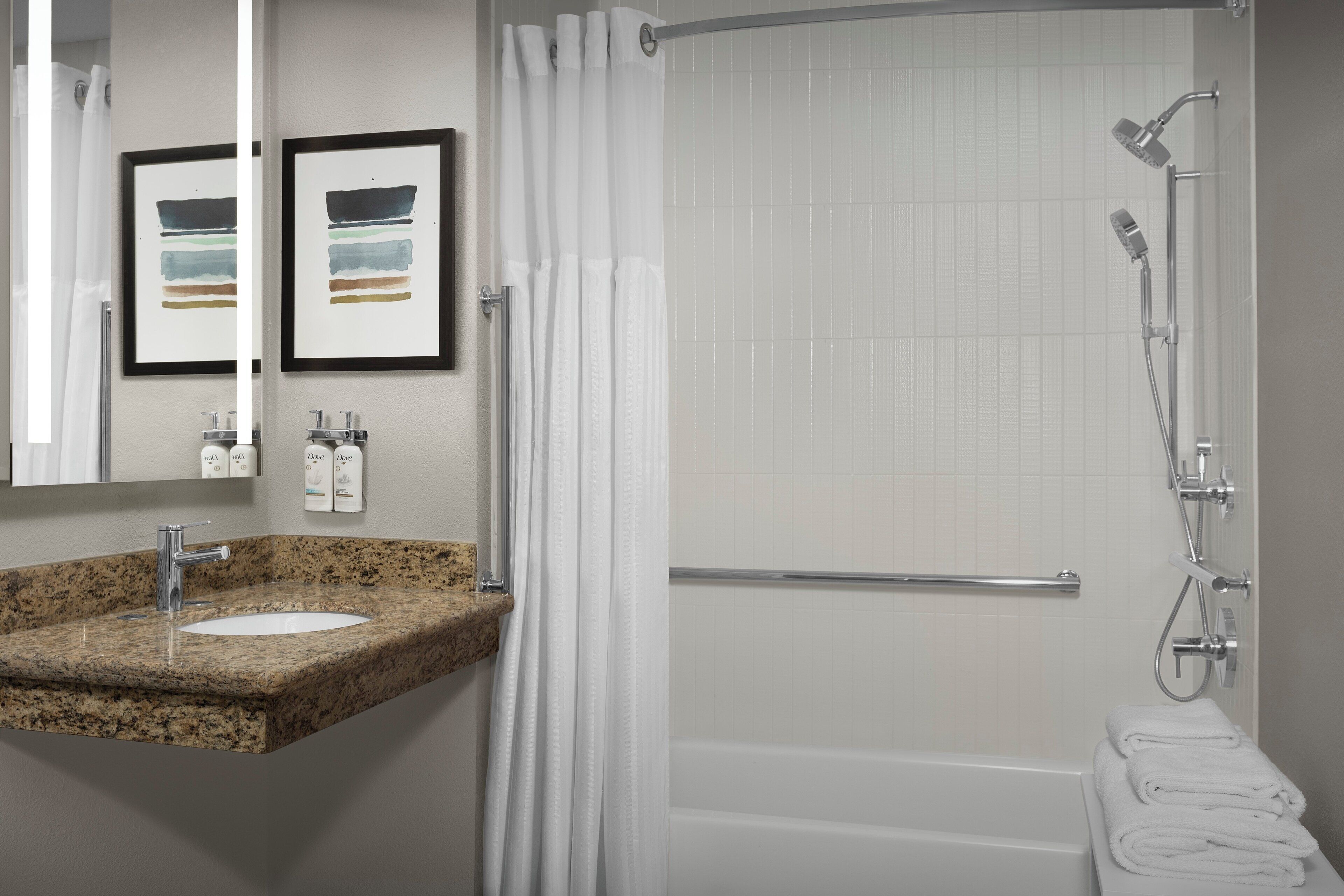 A bathroom with a granite sink, a bathtub, a shower with a handheld showerhead, and a towel rack.