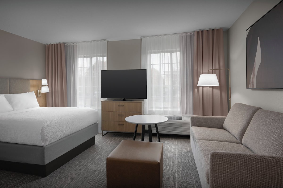 A hotel room with a bed, a sofa, a television, a small table, and a lamp.