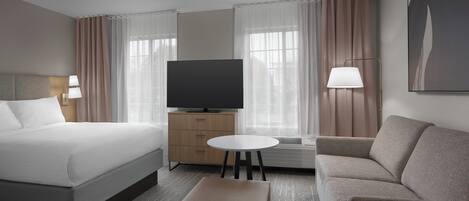 A hotel room with a bed, a sofa, a television, a small table, and a lamp.