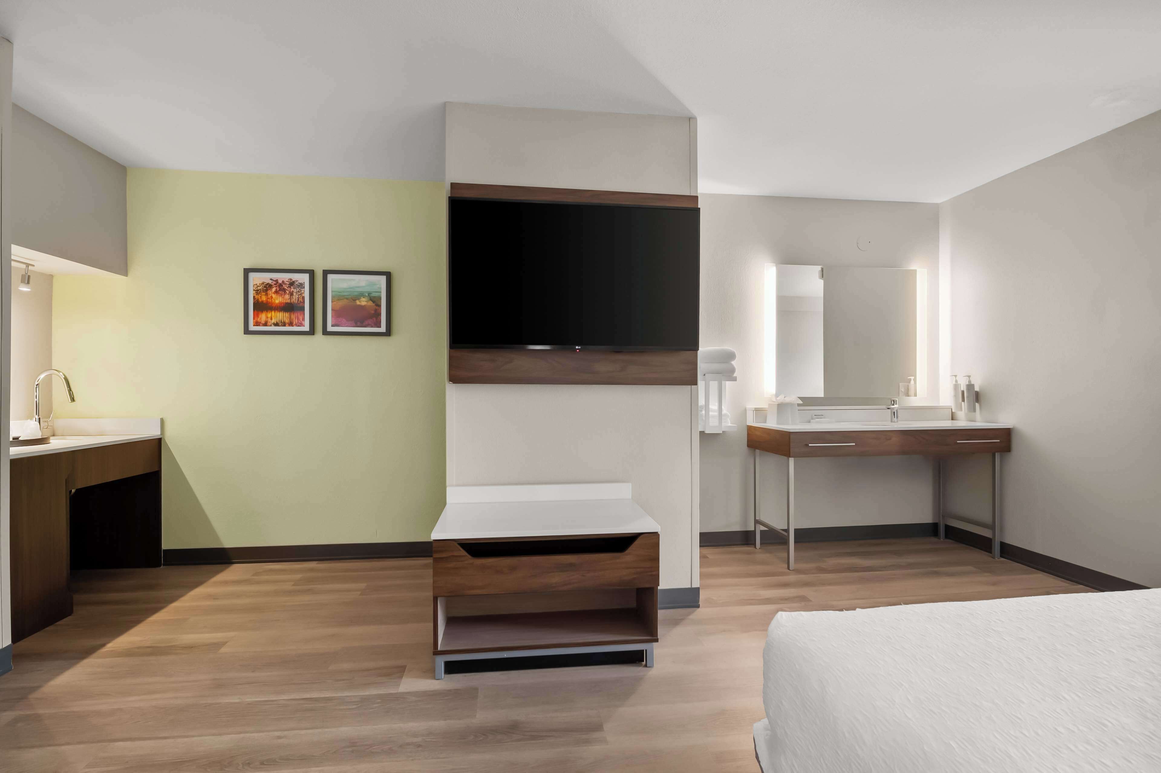 Una habitación de hotel moderna con cama, escritorio con lavamanos, televisor de pantalla plana montado en la pared y un pequeño rincón de descanso.