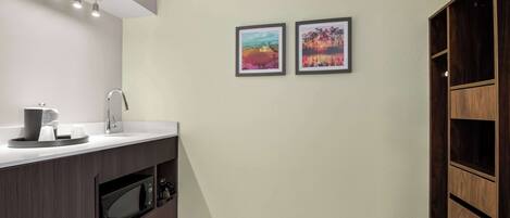 A modern kitchen with a built-in microwave, a sink, and a coffee maker. There are two framed pictures on the wall and a wooden cabinet to the right.