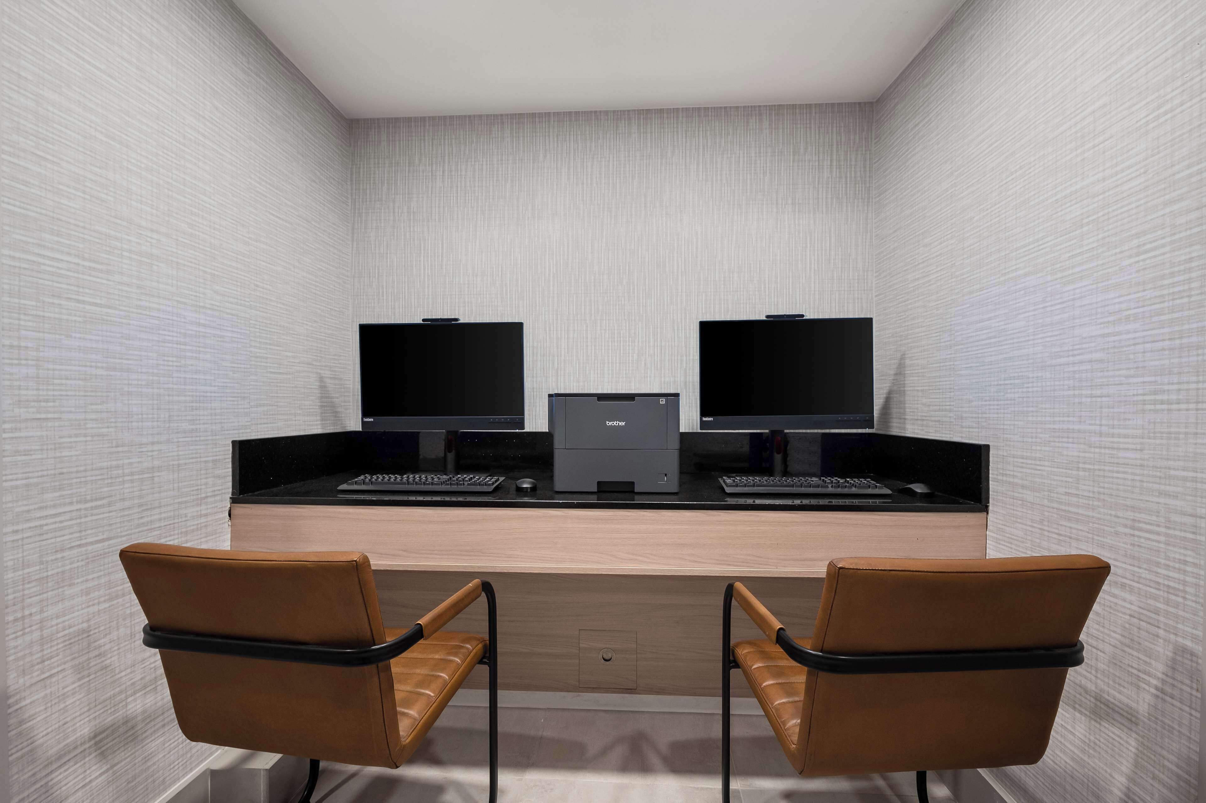 A modern office space with two desks, each with a computer and keyboard, and two leather chairs.