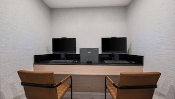 A modern office space with two desks, each with a computer and keyboard, and two leather chairs.