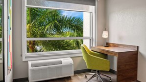 Una habitación con un ventanal grande, un escritorio, una silla y una lámpara de pared.