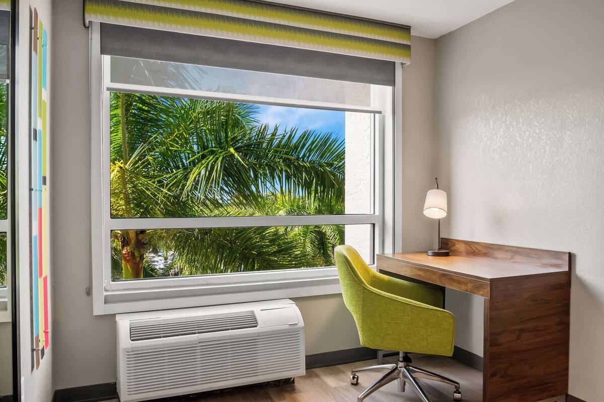 Una habitación con un ventanal grande, un escritorio, una silla y una lámpara de pared.