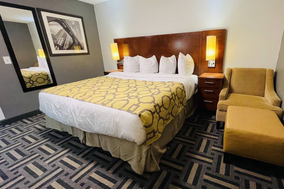 Habitación de hotel con una cama grande, una mesita de noche, una silla, un espejo y dos lámparas fijadas a la pared.