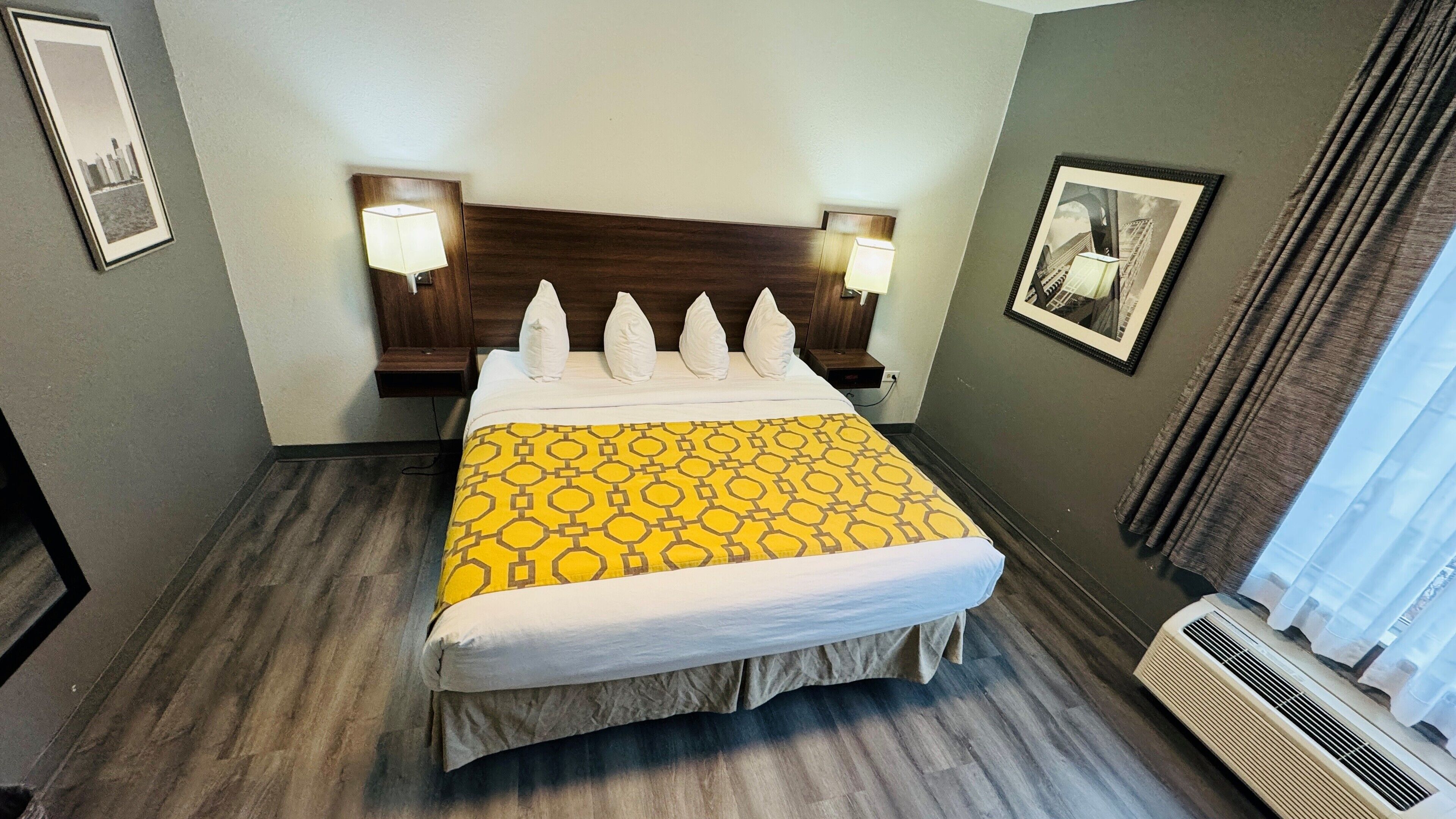 A hotel room with a bed, two bedside lamps, a headboard, a framed picture on the wall, and a window with curtains.