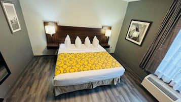 A hotel room with a bed, two bedside lamps, a headboard, a framed picture on the wall, and a window with curtains.