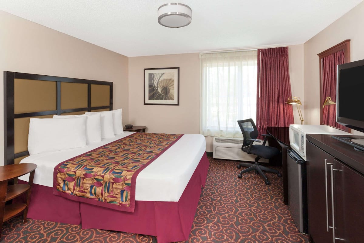 Een hotelkamer met een bed, bureau, televisie en raam met gordijnen.