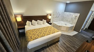 A hotel room with a large bed, a bathroom with a marble wall, and a wooden floor.