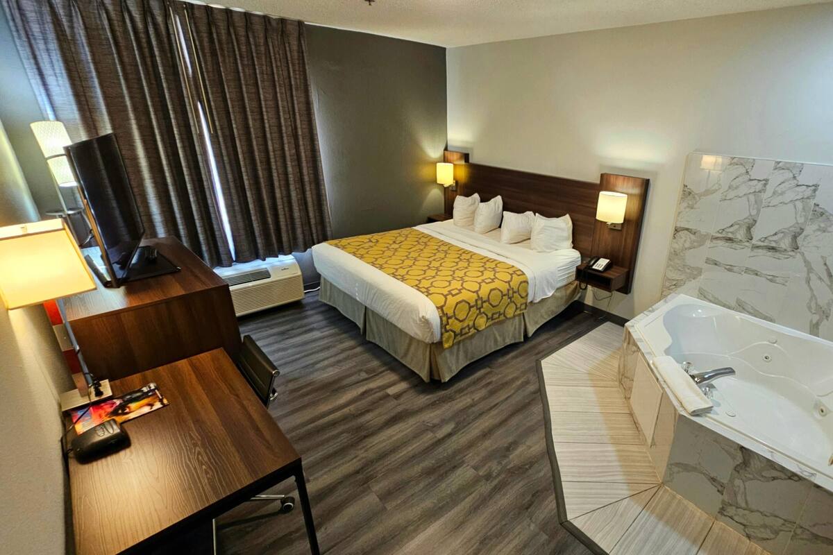 Hotelkamer met een bed, bureau, lamp, televisie en een badkamer met bad en douche.