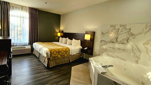 Una habitación de hotel con una cama grande, lámparas de noche, una pared con mosaicos de mármol, una bañera y un escritorio con una silla.