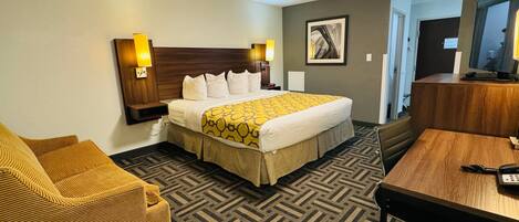 A hotel room with a large bed, a sofa, a desk, and a television.