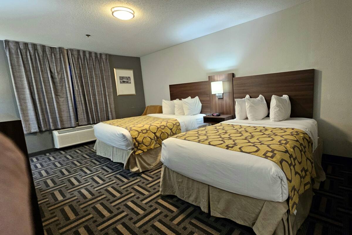 Een hotelkamer met twee bedden, een groot raam met gordijnen, een hoofdeinde met een lamp en een vloerbedekking.