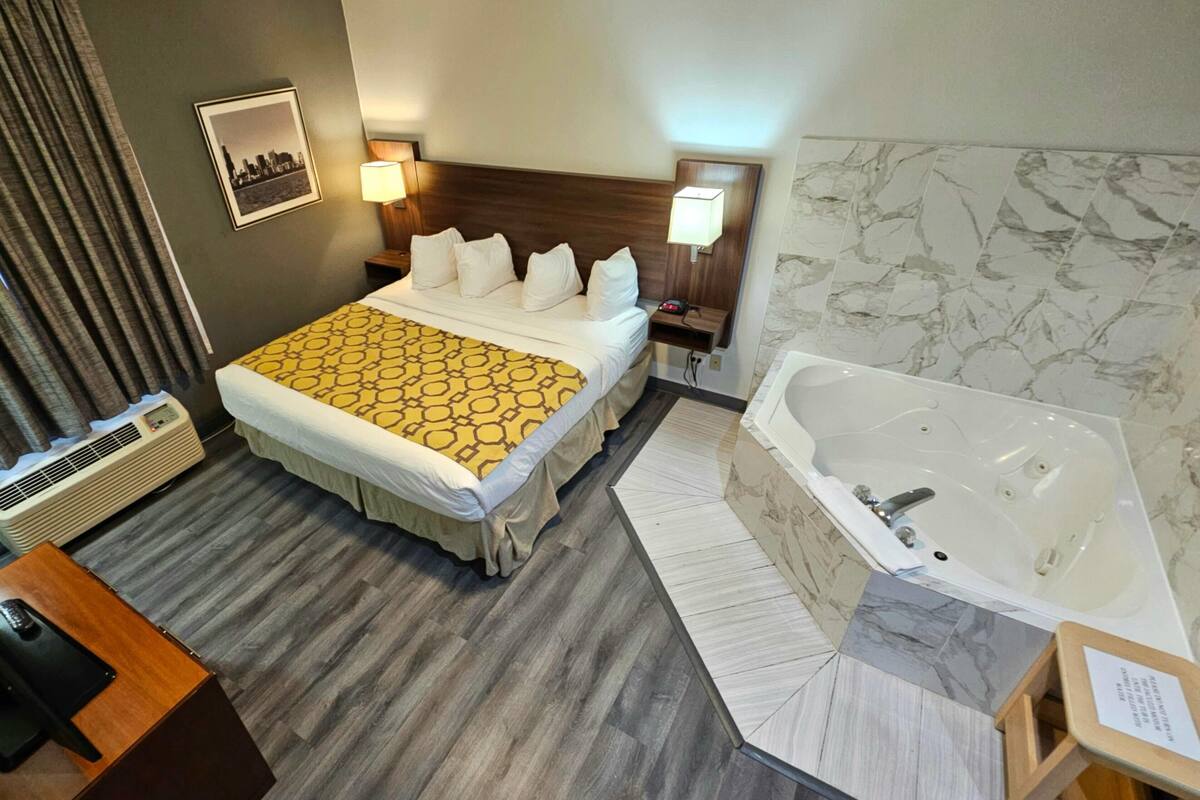 Hotelkamer met een bed, een ruim bad, een bureau met telefoon en een luchtverkoeler aan de muur.