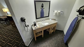 Une petite salle de bain d’hôtel comprenant un lavabo, un miroir, un porte-serviettes et un sèche-cheveux.