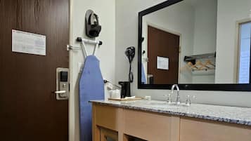 A bathroom with a wooden vanity, a large mirror, a hairdryer, and a towel rack.